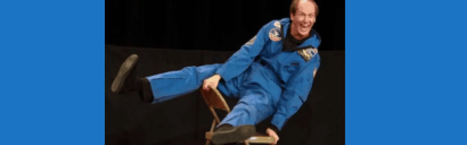 man in blue jumpsuit holding himself off a chair